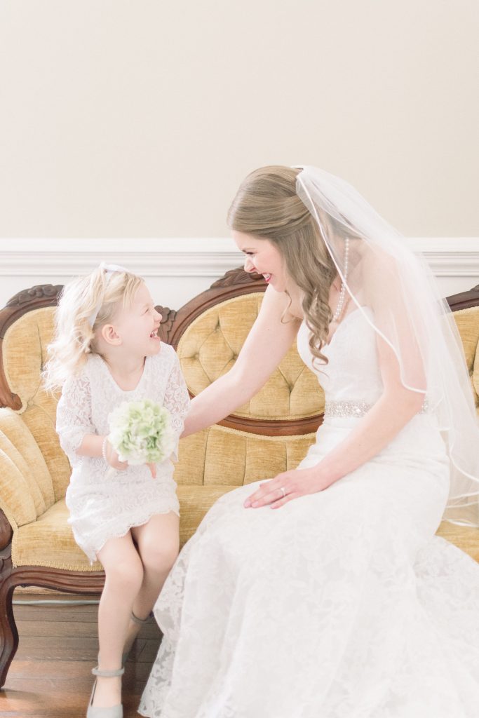 Wedding Photographer in Charlotte NC South Park Forrest Hill Church bride shares a laugh with flower girl on yellow antique couch