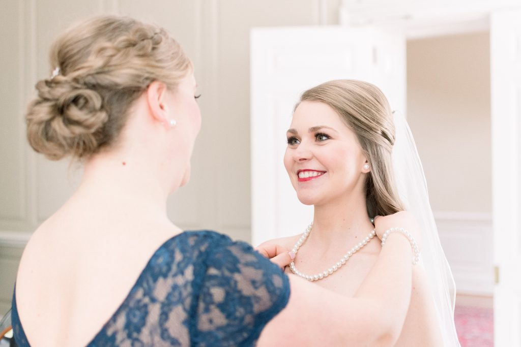 Wedding Photographer in Charlotte NC South Park Forrest Hill Church bridesmaid putting on pearl necklace on bride